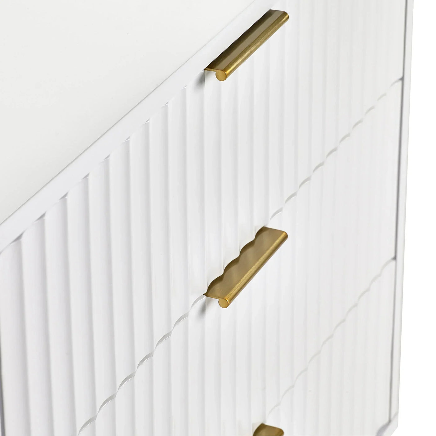 White chest of drawers with ribbed fronts and gold metal handles, close-up view