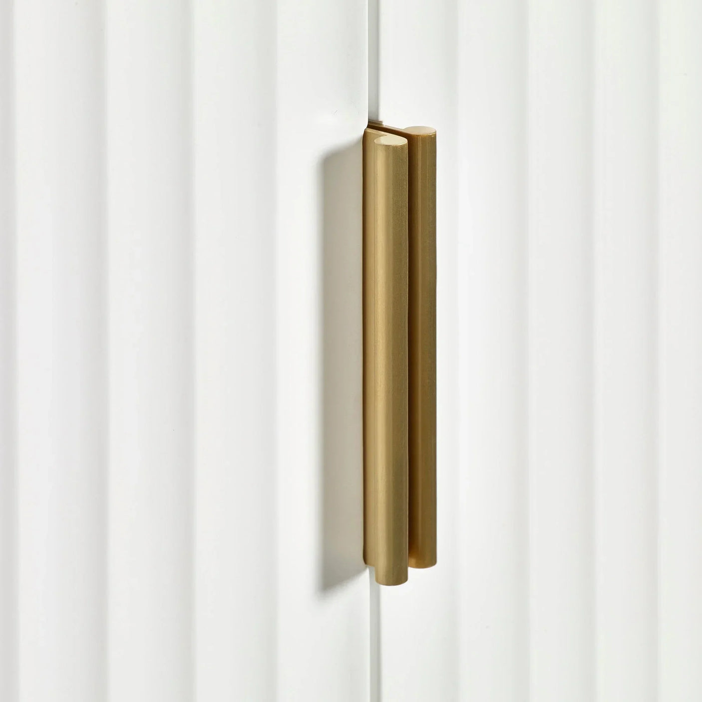 Close-up of gold metal cabinet handle on white textured furniture door