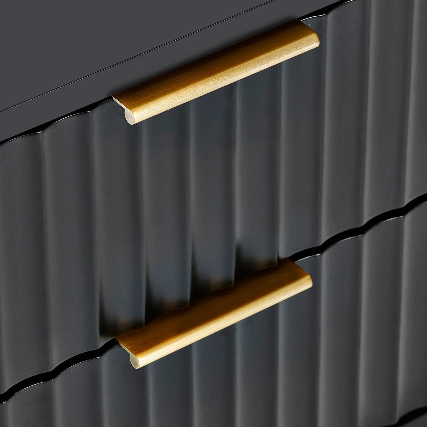 Black chest of drawers with gold handles and fluted front detail, close up