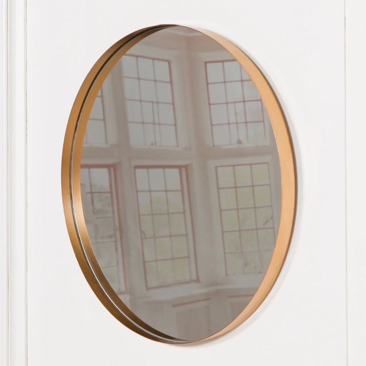 Round wall mirror with slim gold metal frame on white background