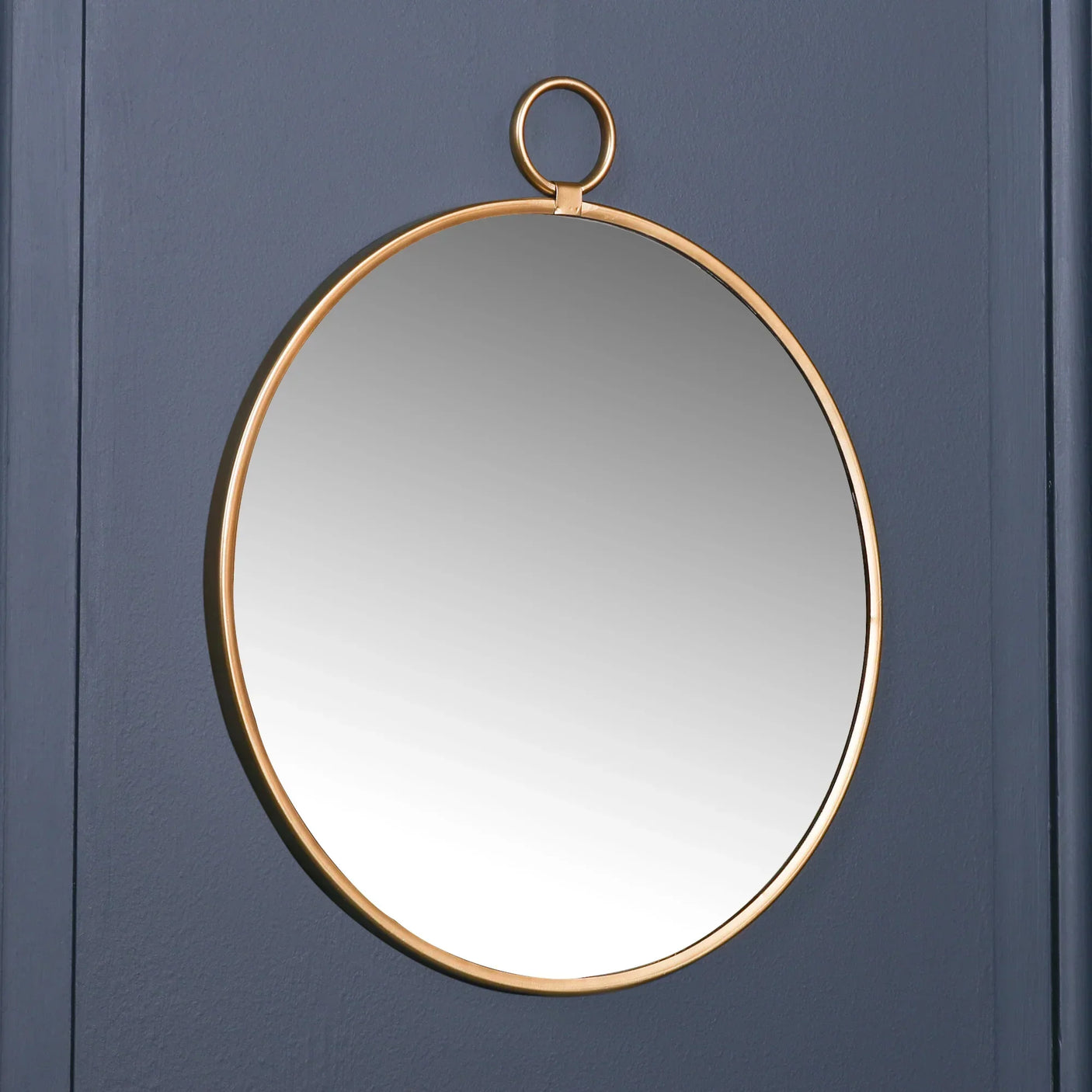 Round gold wall mirror with hanging ring on dark blue panelled background