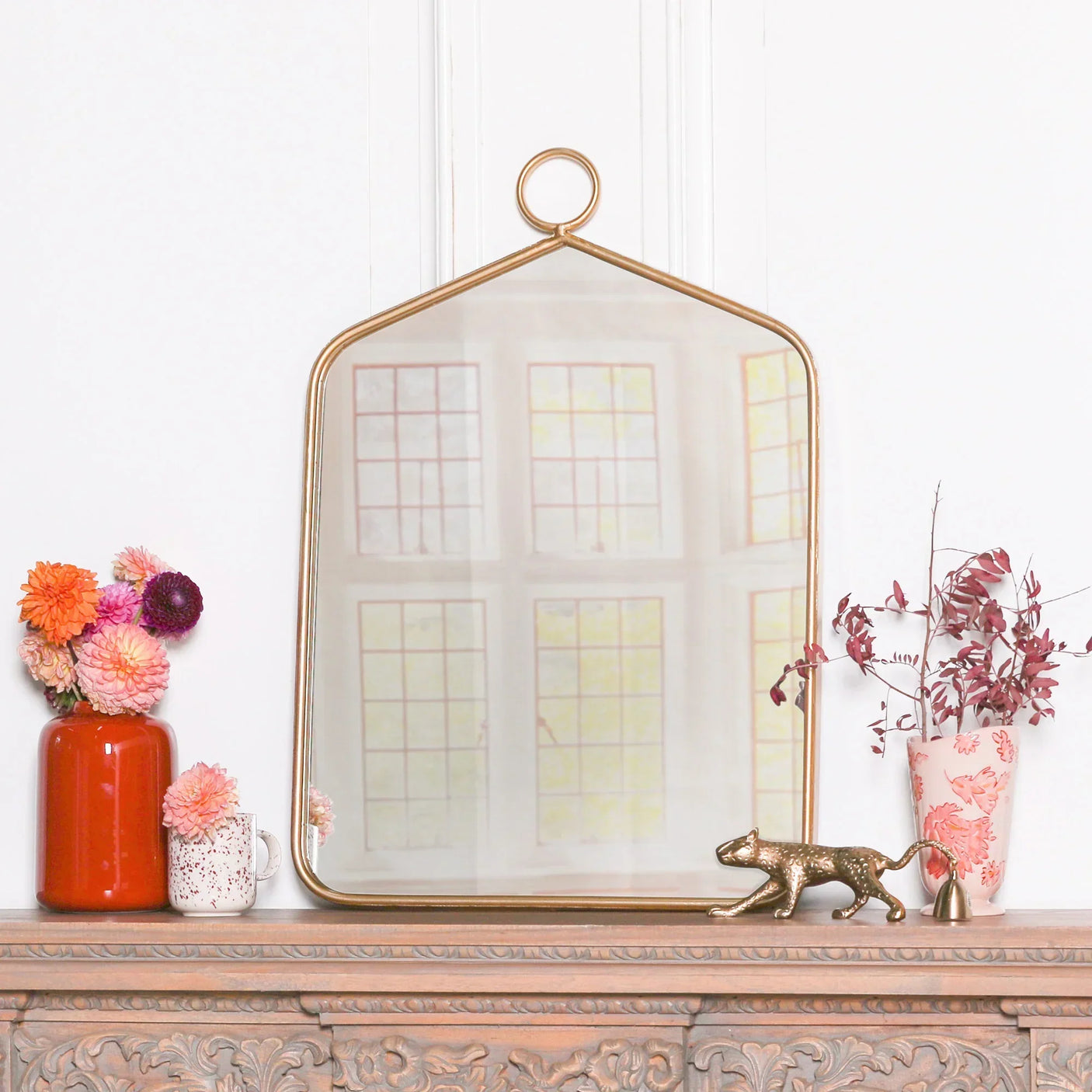 Gold framed arched wall mirror on mantel with vases and floral arrangement