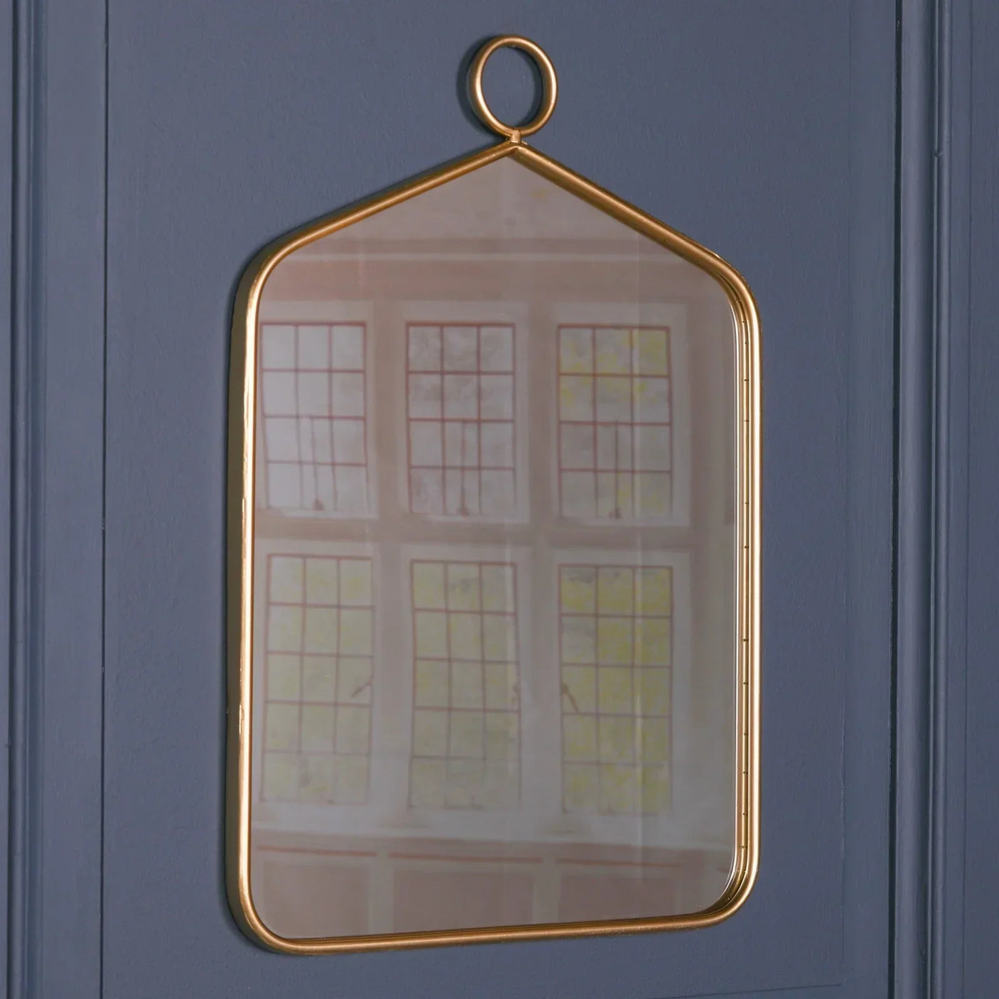 Rectangular wall mirror with gold metal frame and loop detail on blue wall