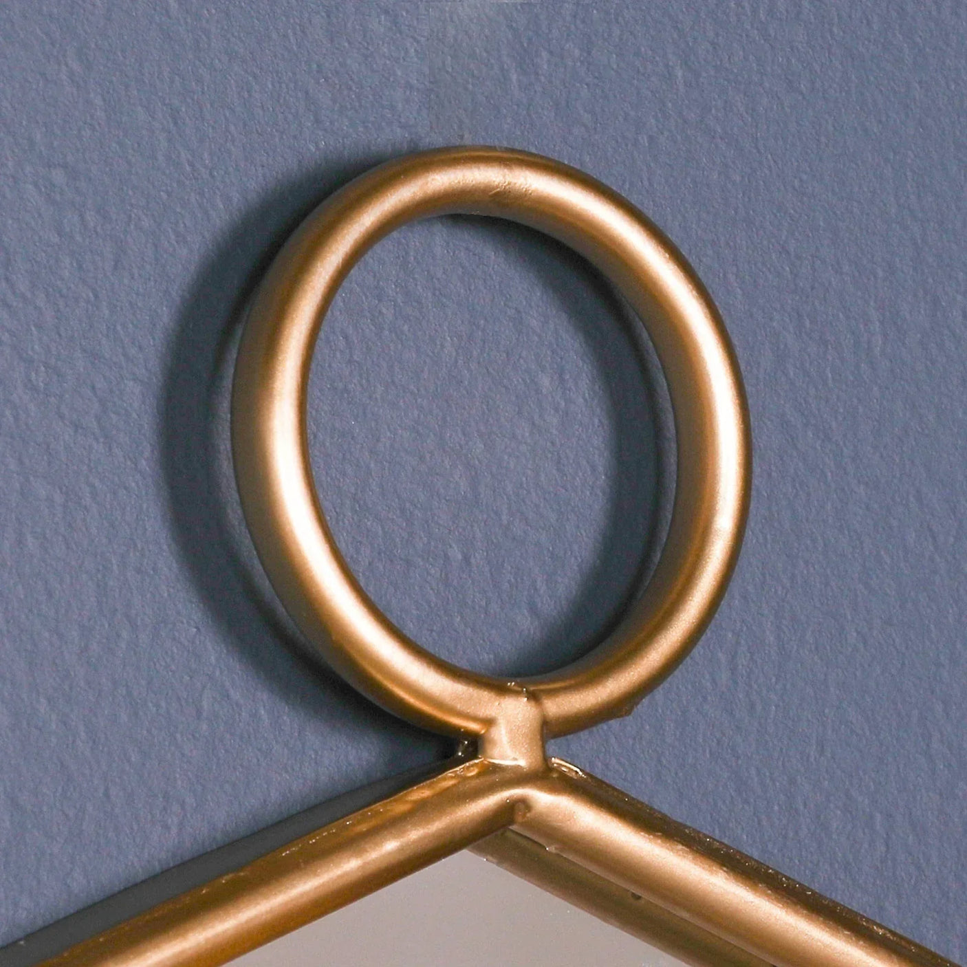Gold metal mirror hanging loop detail against blue painted wall