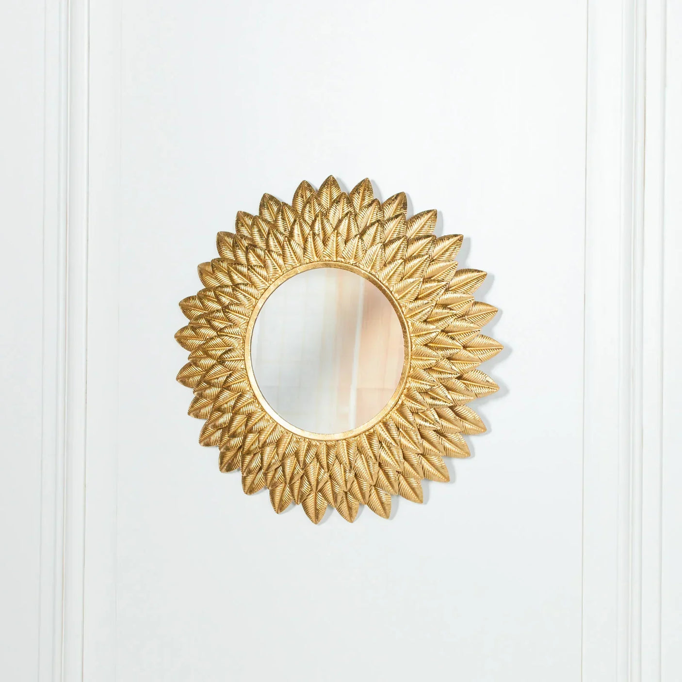 Gold sunburst wall mirror with textured frame on white panelled wall