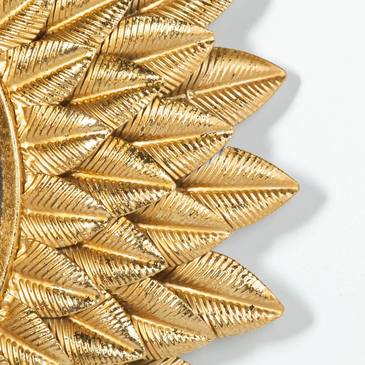 Gold metal wall mirror frame with textured leaf pattern, close-up corner view