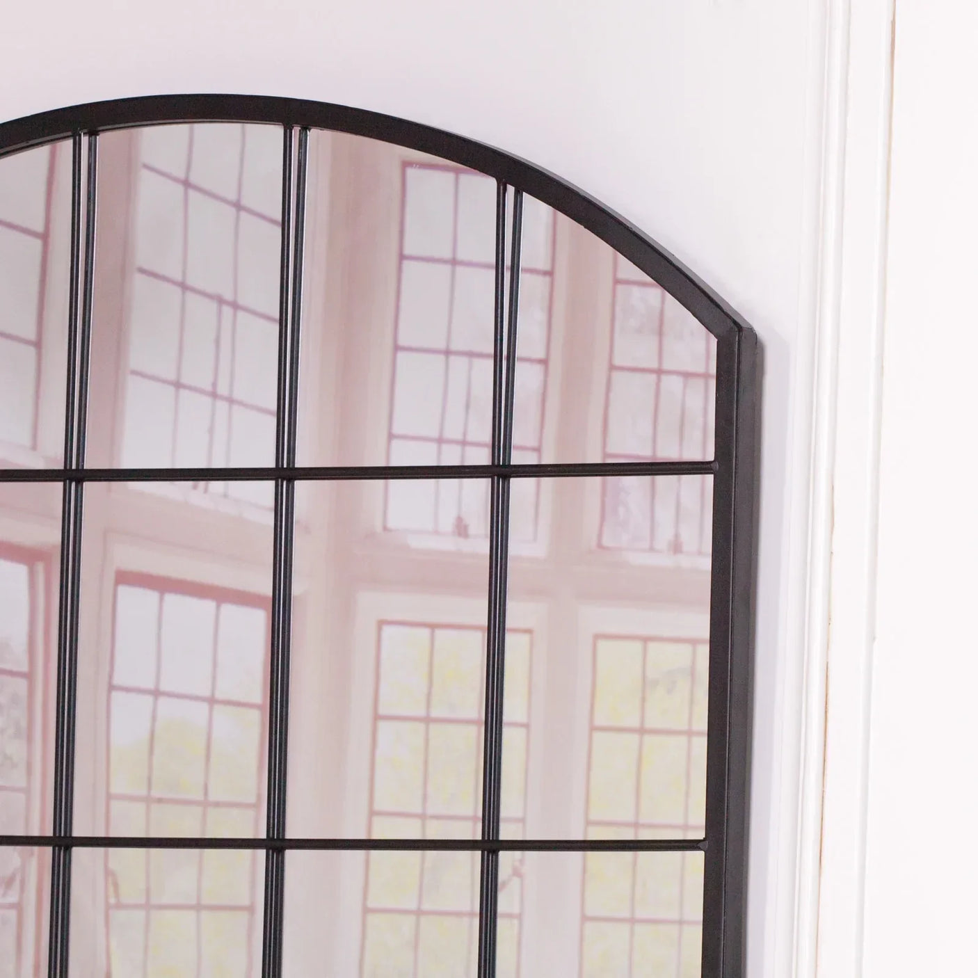 Arched black metal window mirror with grid design reflecting window light