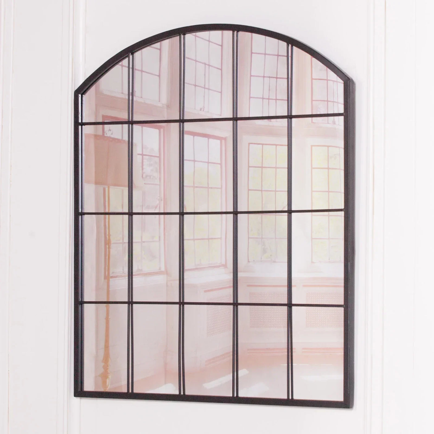 Arched wall mirror with black metal frame and windowpane design on white wall
