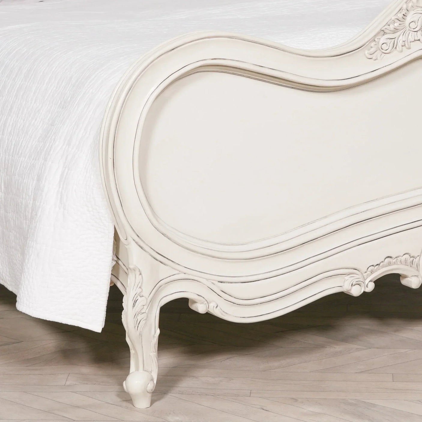 Cream wood bed frame with carved detailing and white quilted bedding on herringbone floor