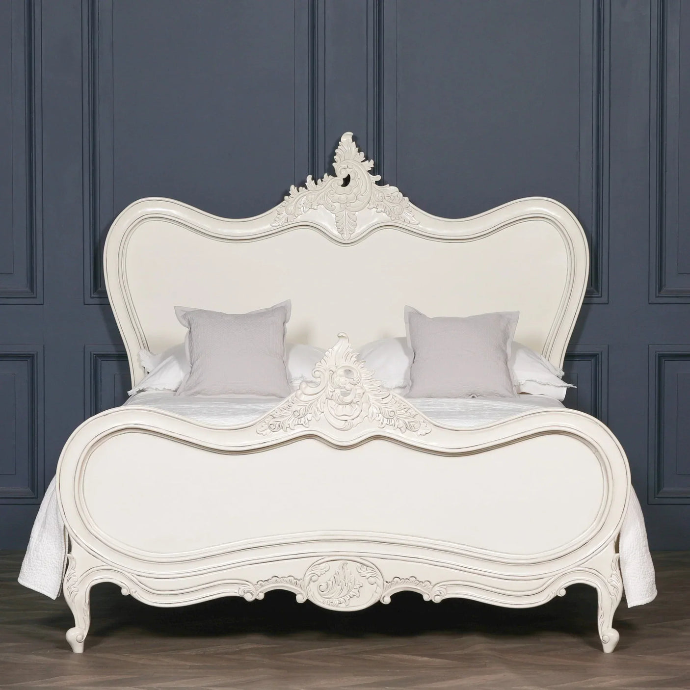 French style cream bed with ornate carved headboard and footboard against dark wall