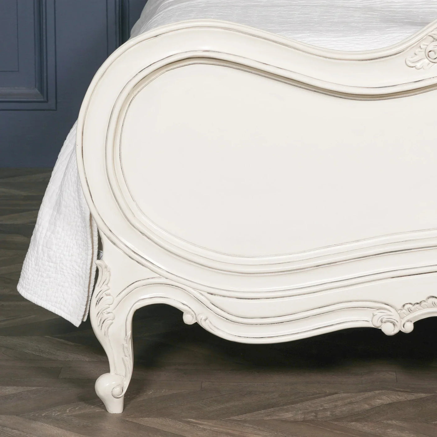 Ivory painted wooden bed frame with curved detailing and carved legs on wood flooring