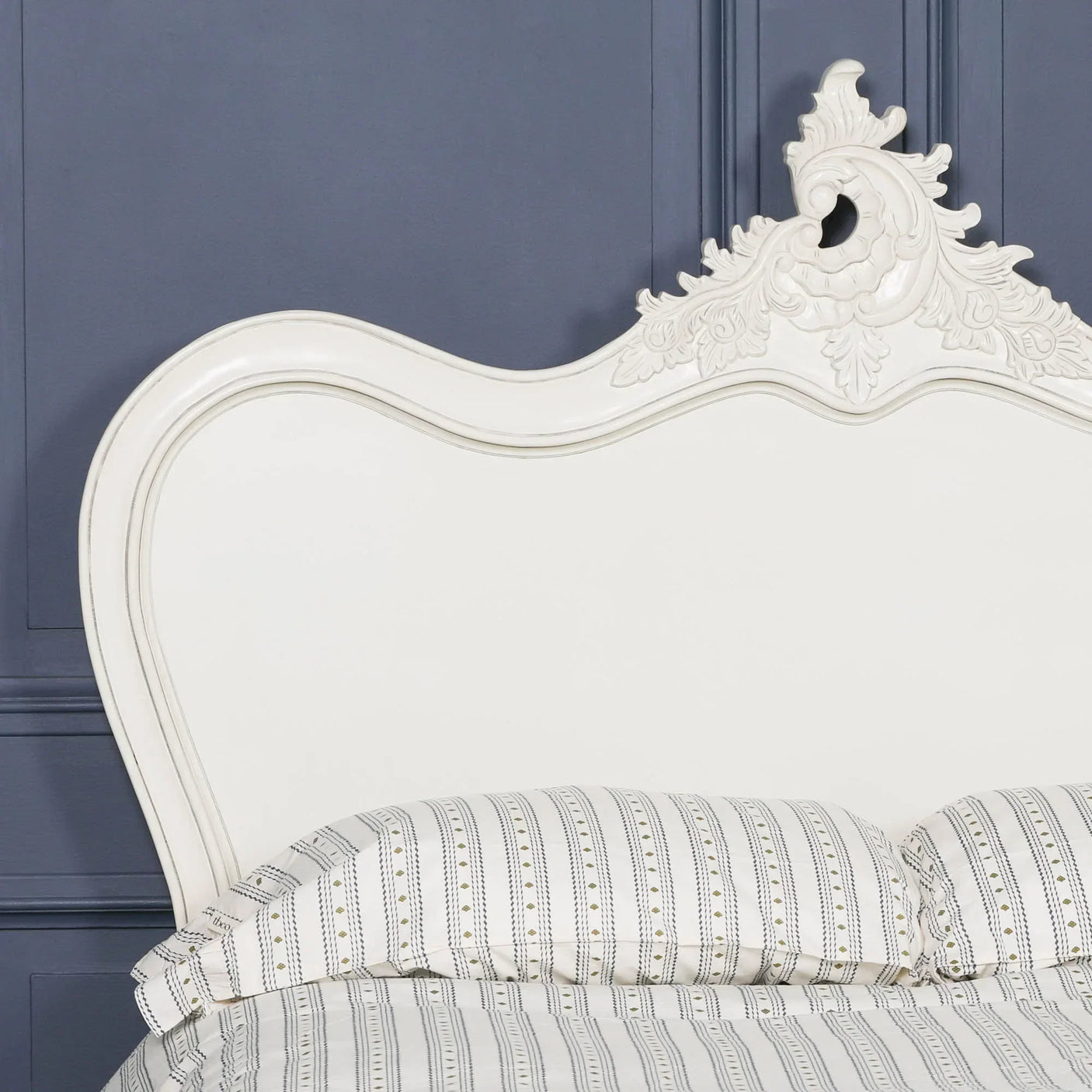 White wooden bed frame with ornate carved headboard and striped bedding against blue wall