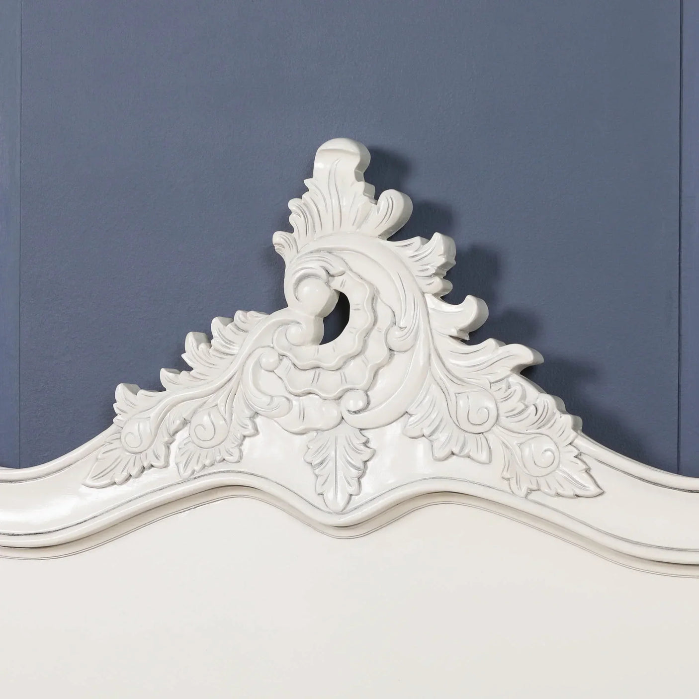 White carved wood headboard with ornate floral detailing against blue wall