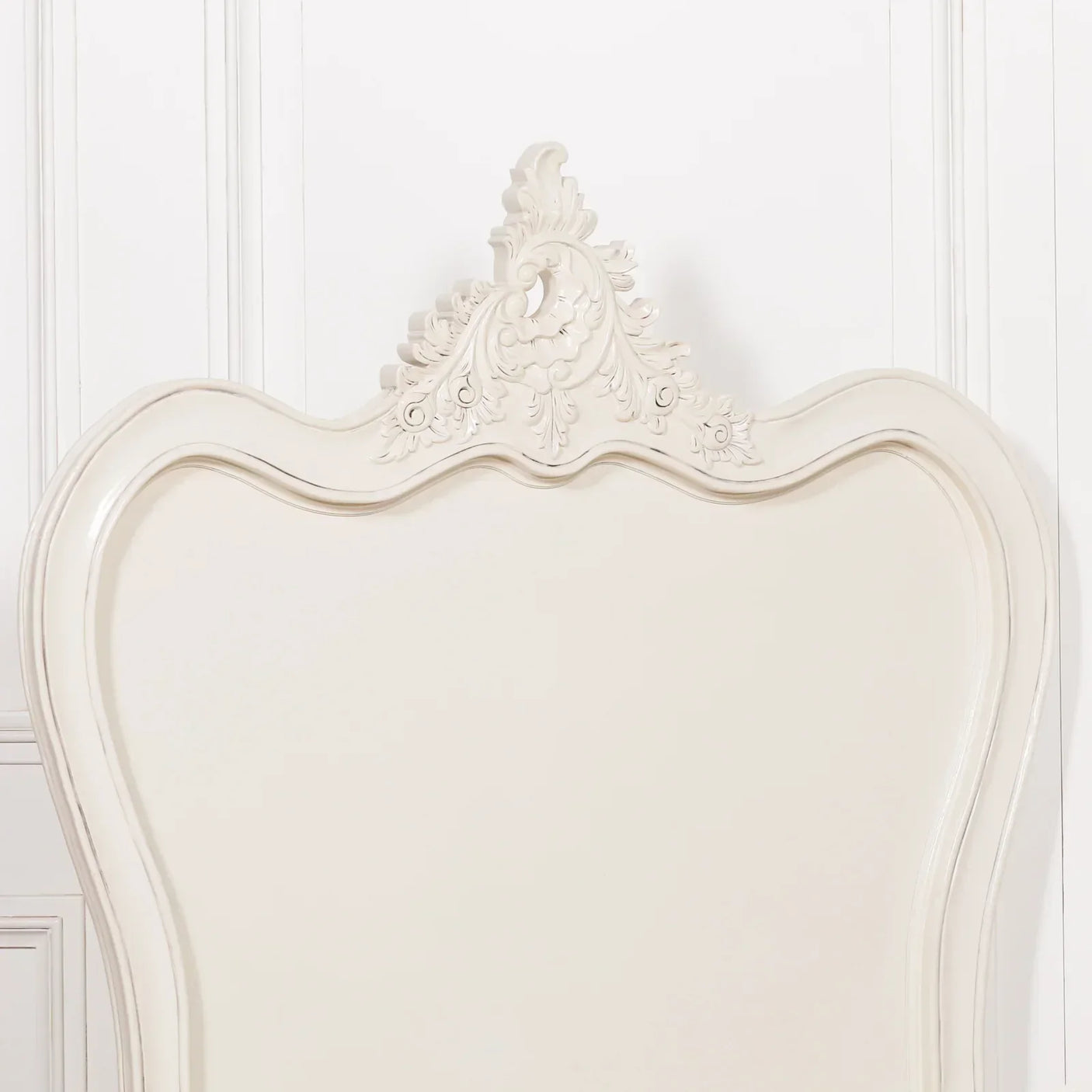 Cream wooden bed headboard with ornate carved detailing against white wall