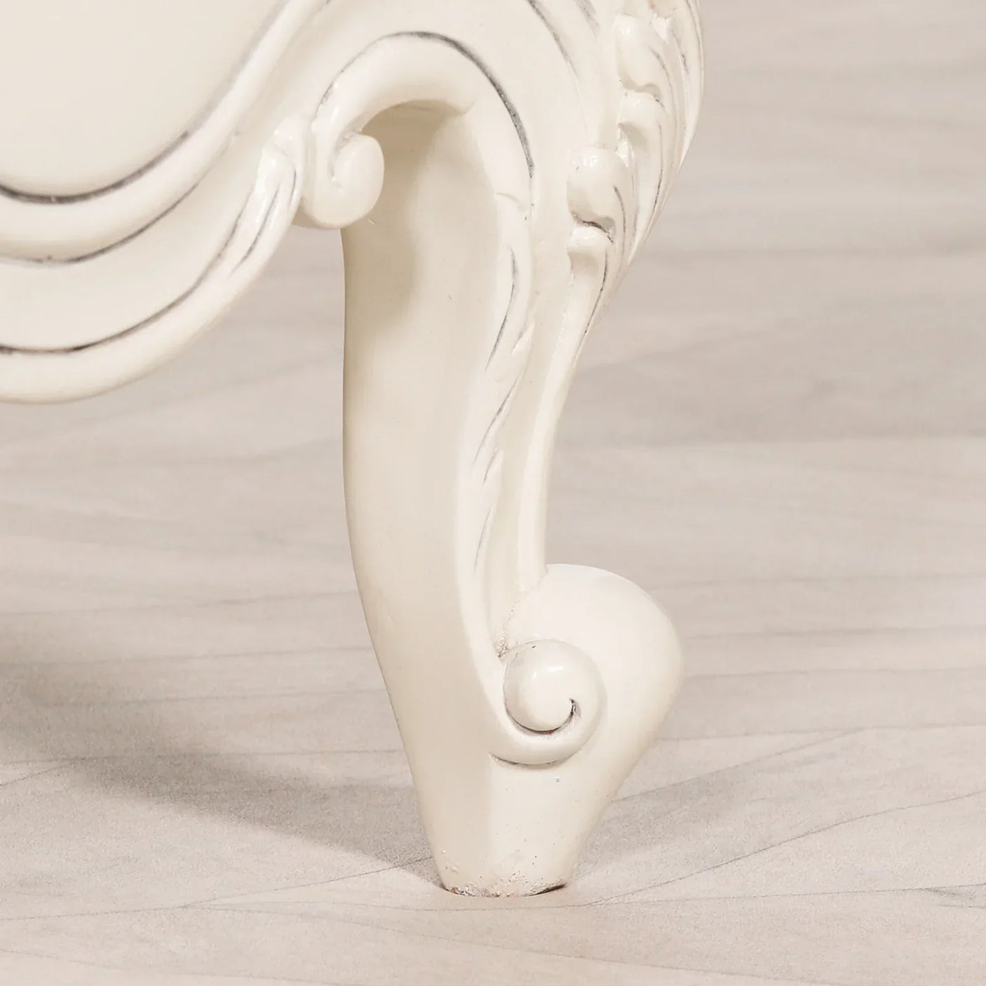 Carved white wooden furniture leg with scroll detail on light floor
