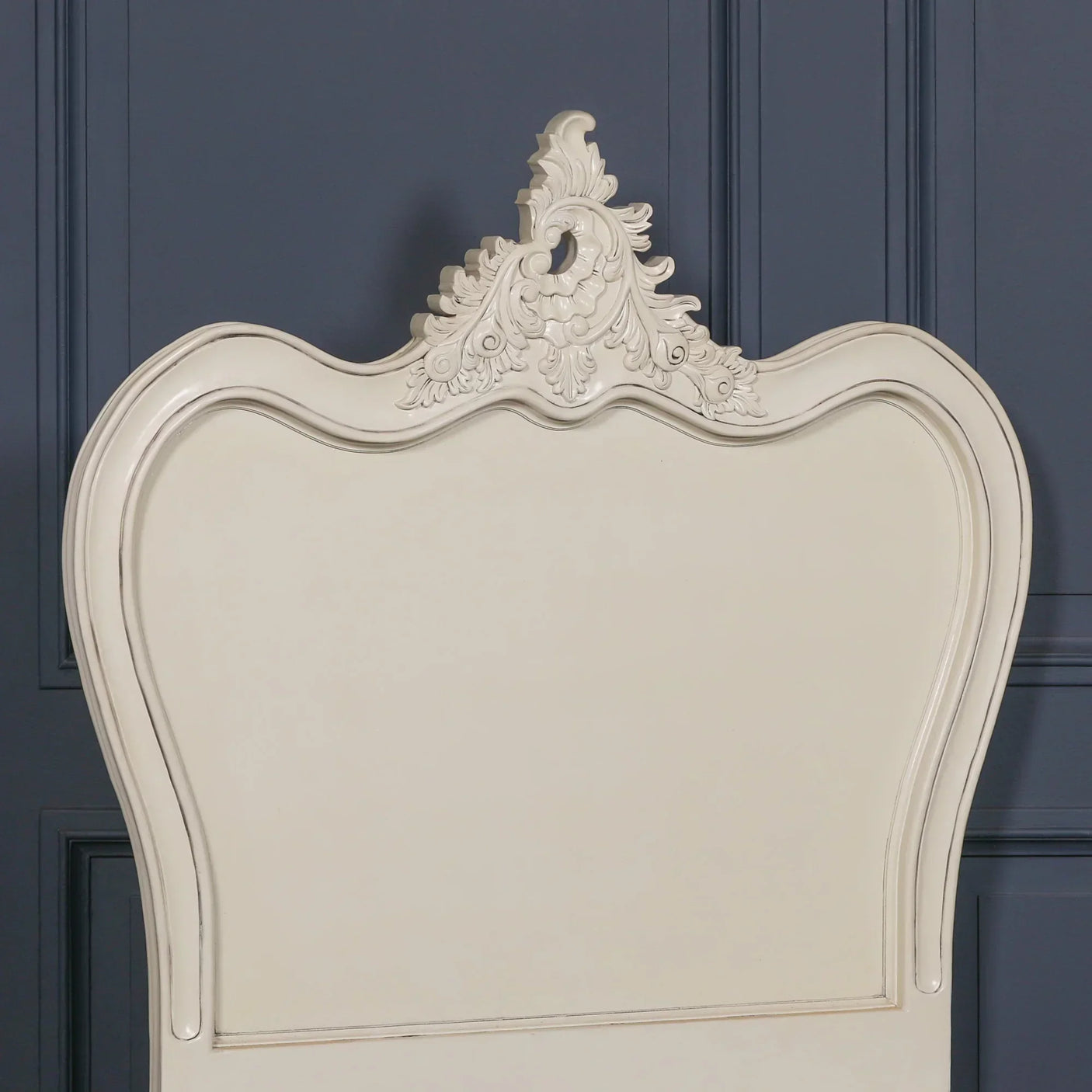 Cream painted wooden headboard with ornate carved detailing against blue panel wall