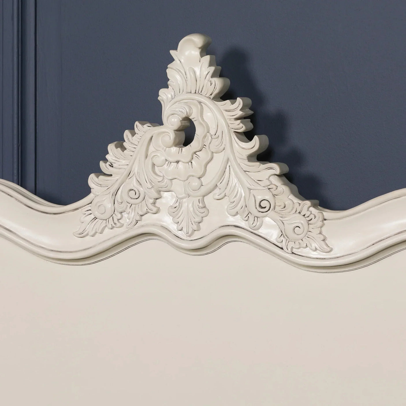 cream wooden headboard with ornate carved detailing against dark blue wall