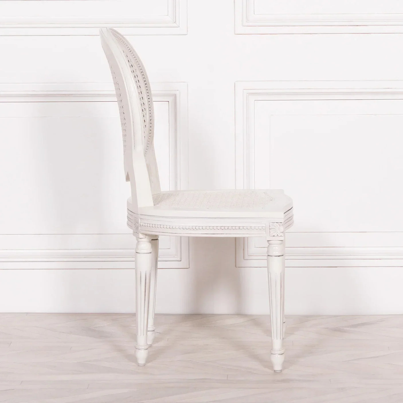 White wooden dining chair with carved legs and woven cane seat, side profile view