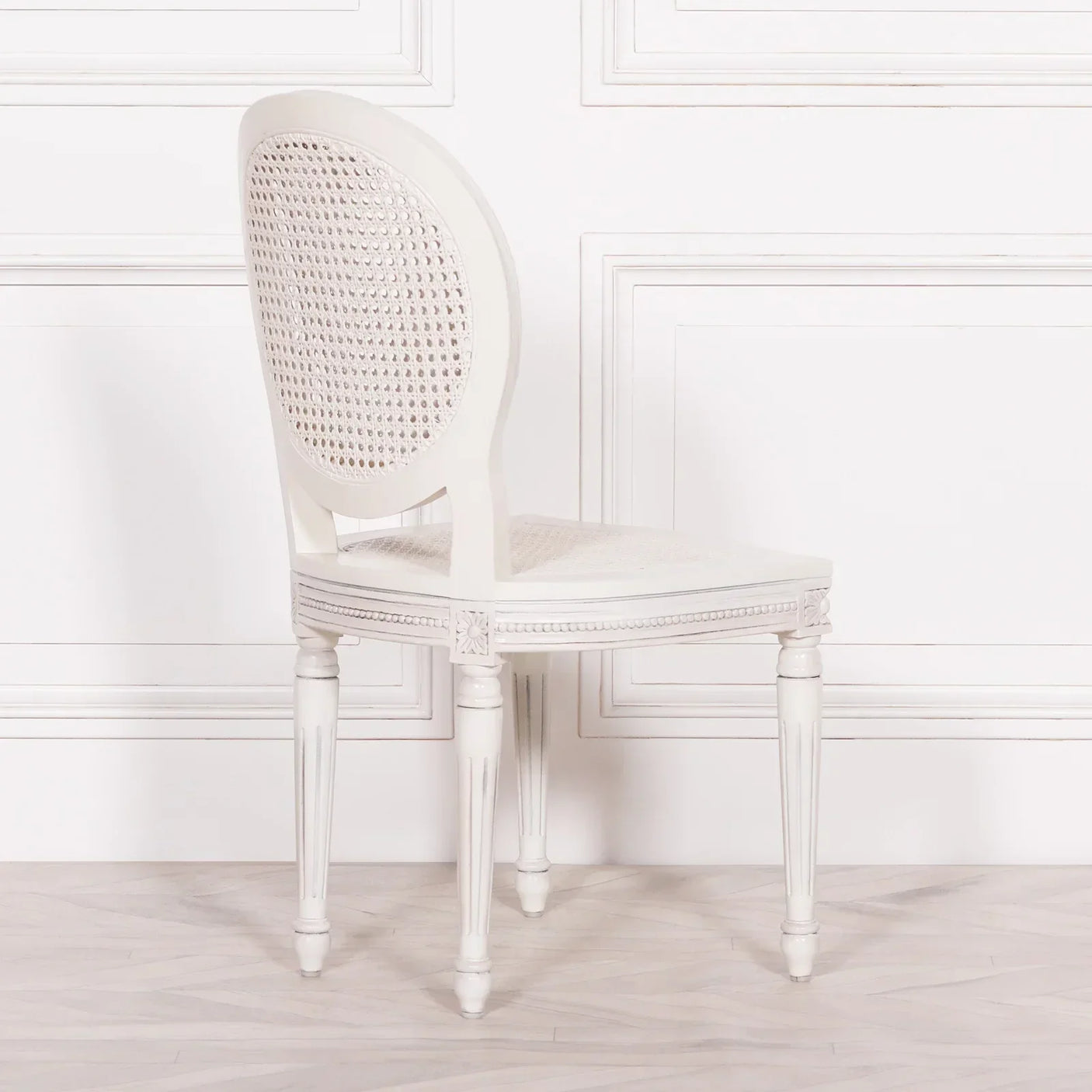 White dining chair with cane backrest and carved wooden legs on light wood floor
