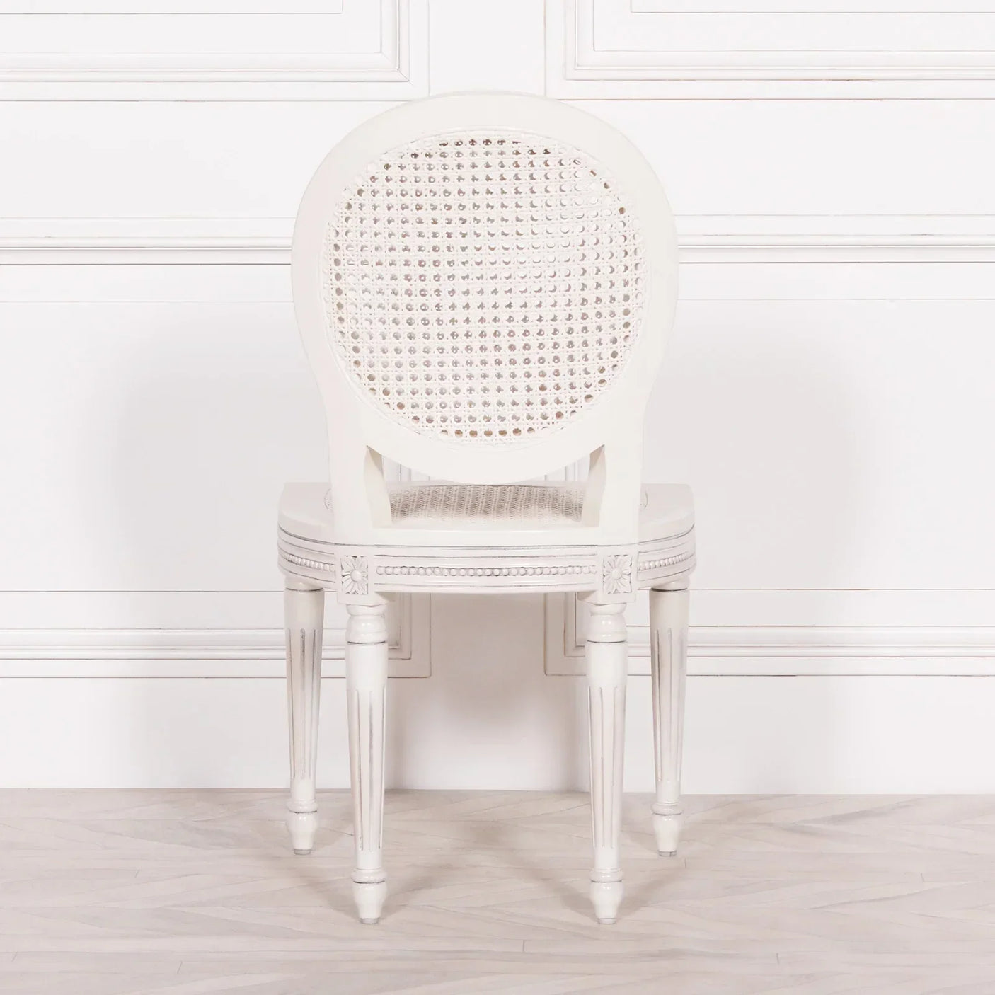 White dining chair with round cane backrest and carved wooden legs, rear view