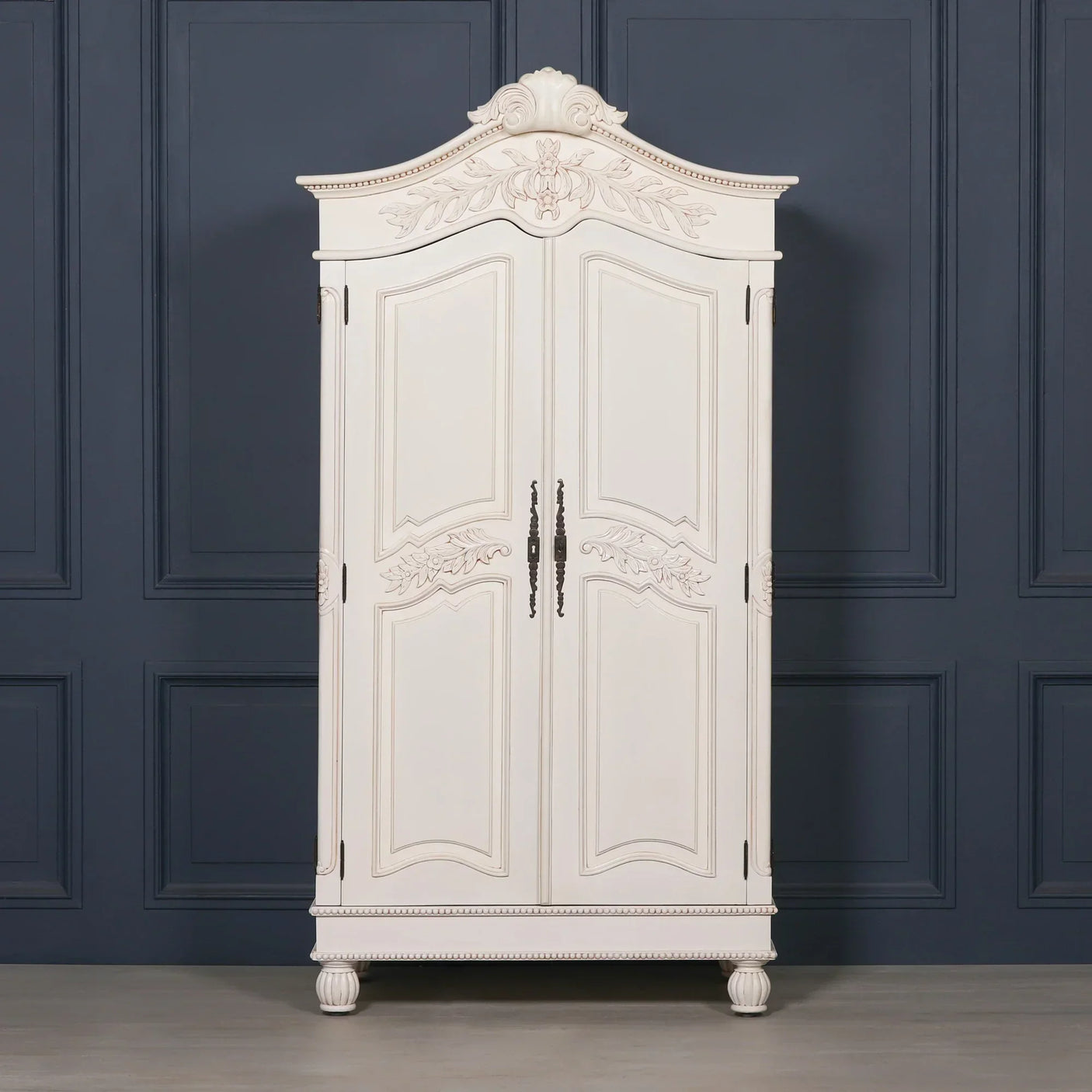 White wooden wardrobe with ornate carved detailing and double doors against dark panel wall