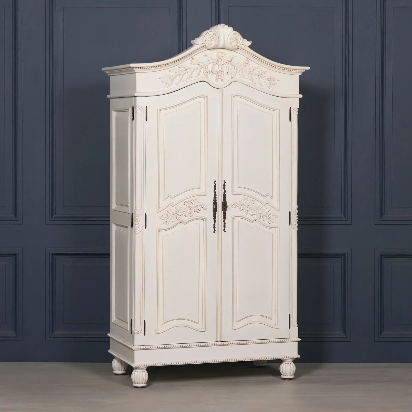 White wooden wardrobe with ornate carved detailing and double doors against navy panel wall