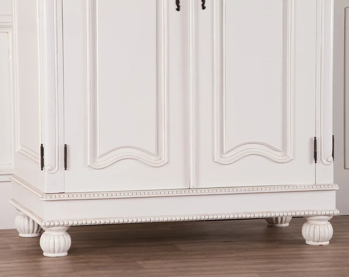 White wooden wardrobe base with carved legs and decorative beading on timber floor