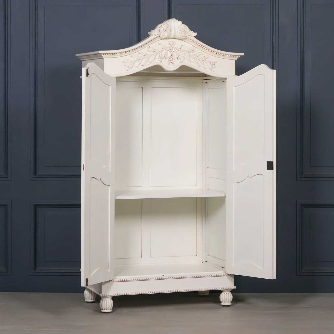 White wooden wardrobe with ornate carved detailing and open double doors against navy wall