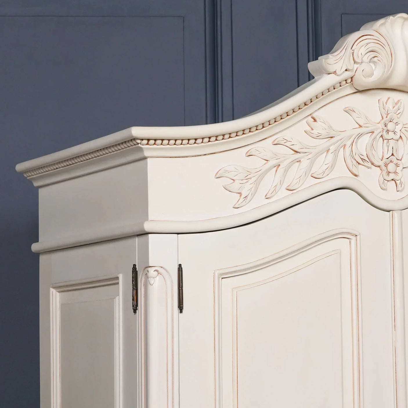 Cream wooden wardrobe with floral carved detail and ornate molding on top corner view