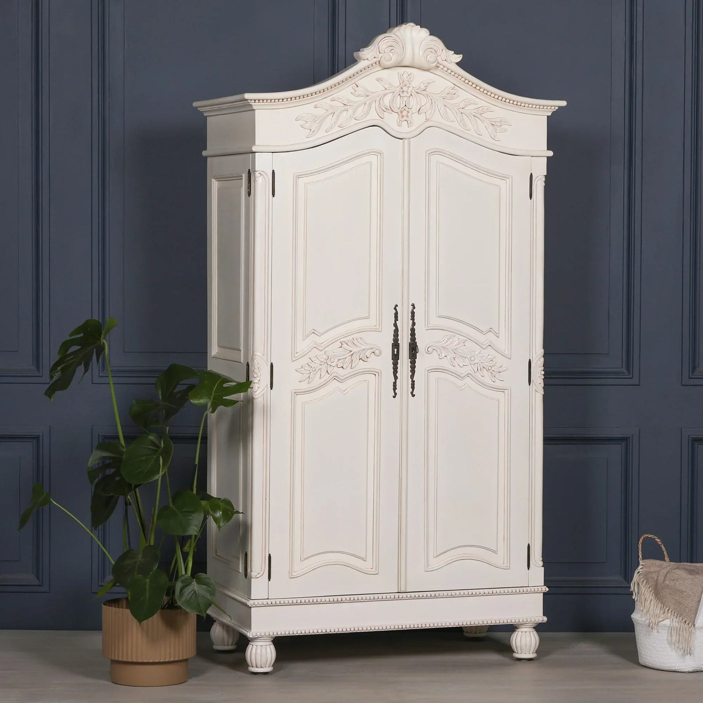 Cream wooden wardrobe with ornate carved details and double doors against dark blue wall