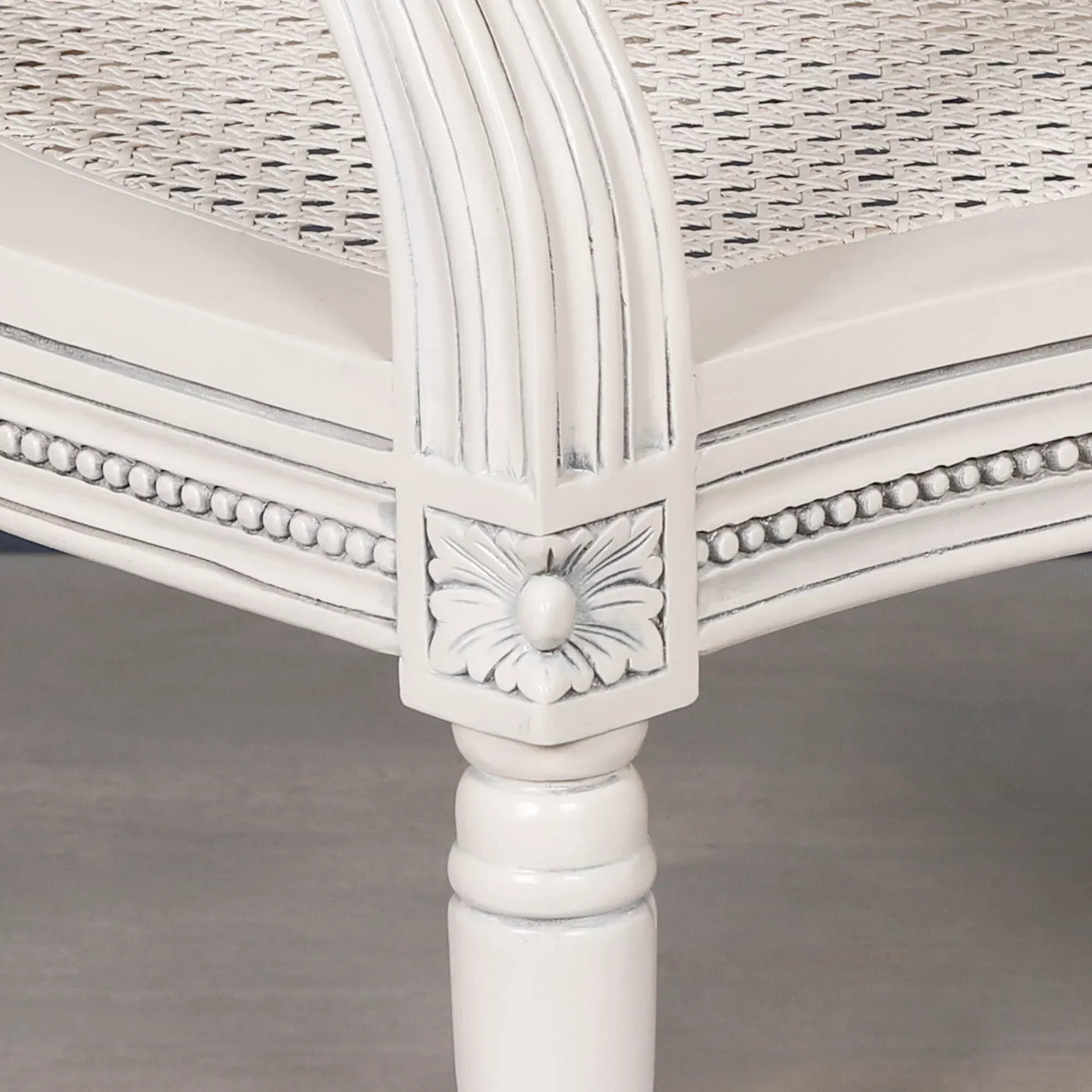 White wooden armchair leg with carved floral detail and cane seat