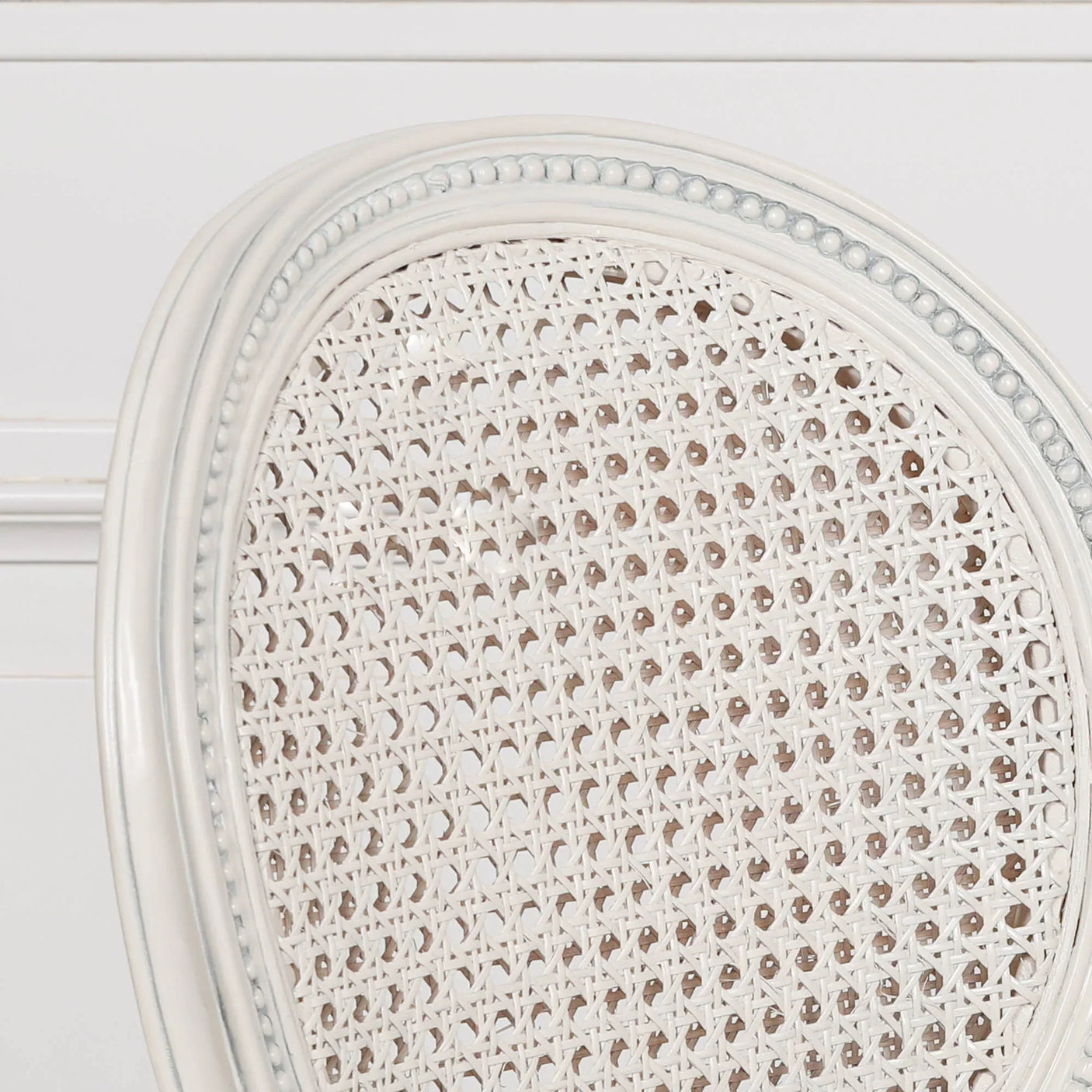 Closeup of cream cane dining chair backrest with carved wood frame