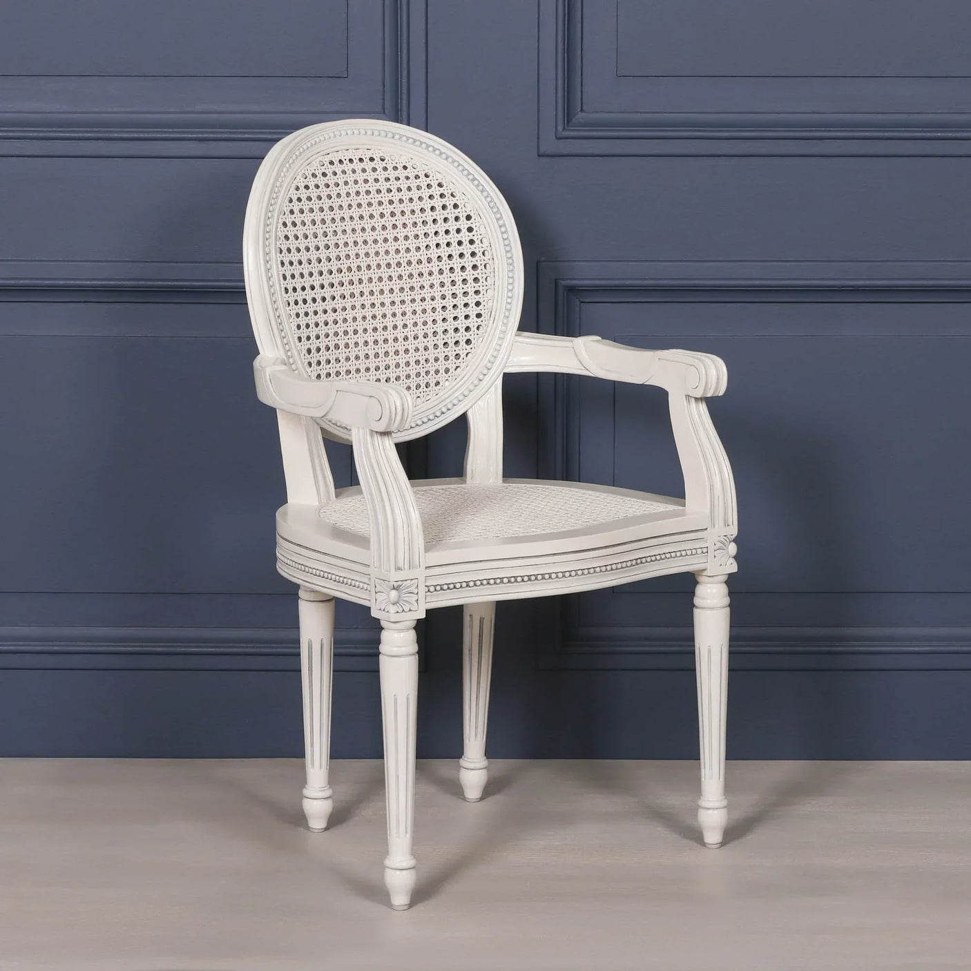 White wooden dining chair with cane backrest and armrests against blue panel wall