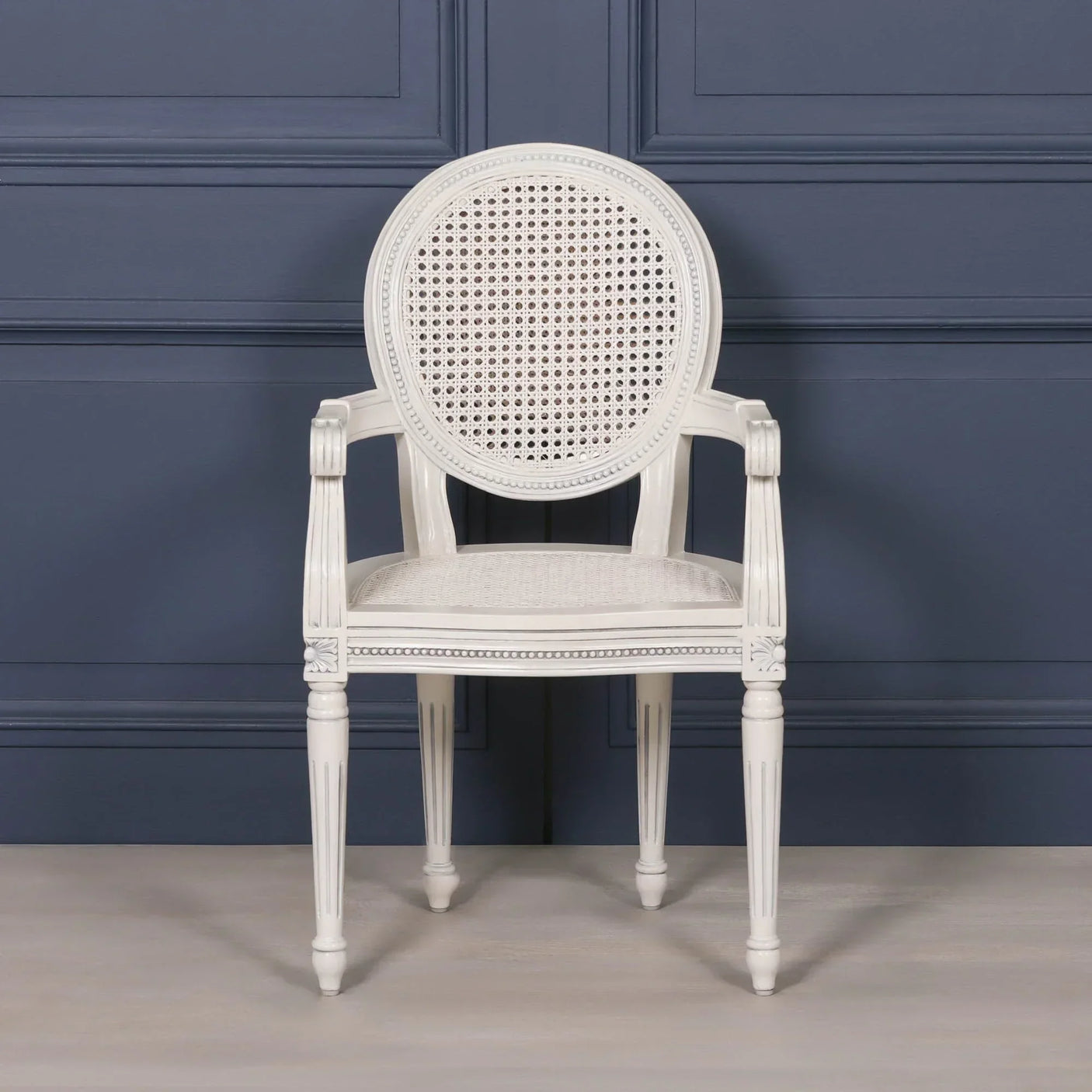 White cane back dining chair with carved wood arms and legs against blue paneled wall