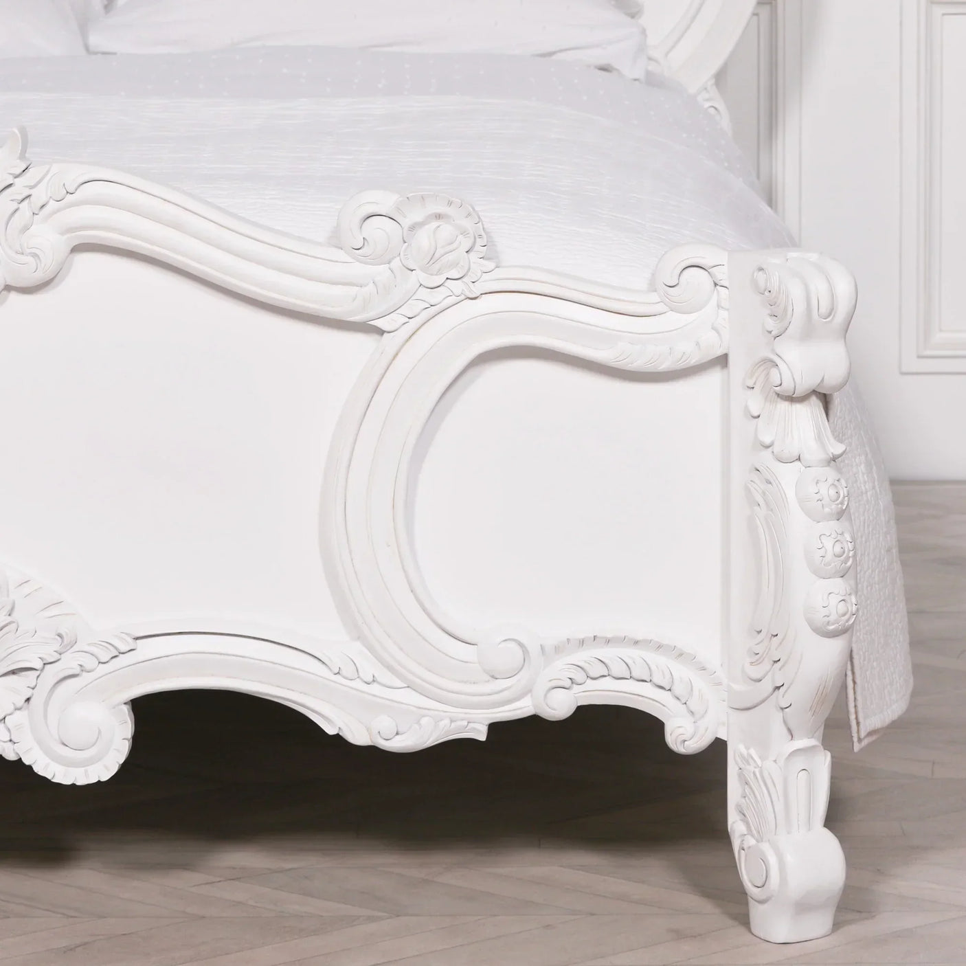 White carved wooden bed frame with ornate detailing and curved legs on hardwood floor