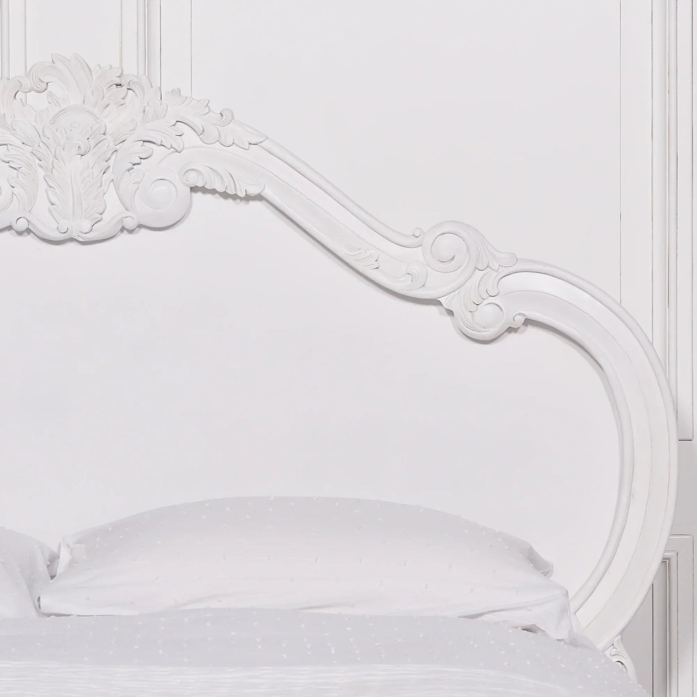 White carved wooden bed frame with ornate headboard detail and white bedding