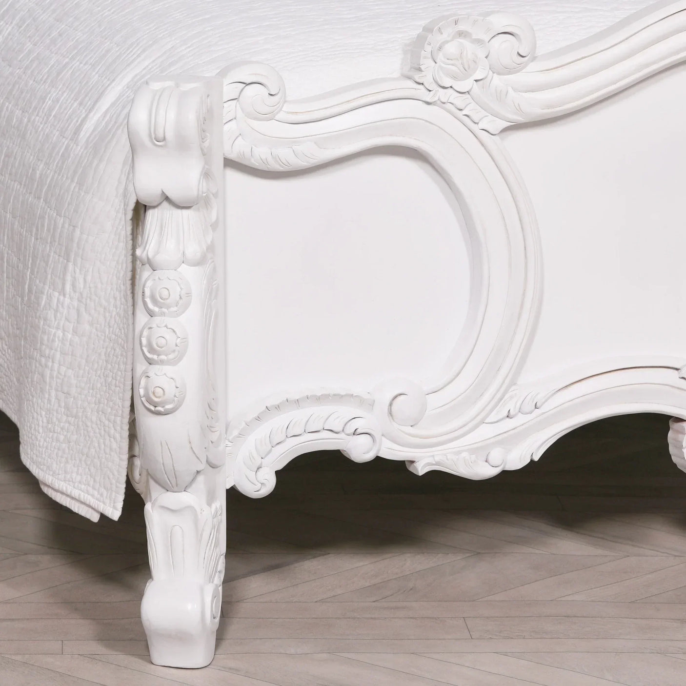 carved white wooden bed frame with floral detailing and curved leg on parquet floor