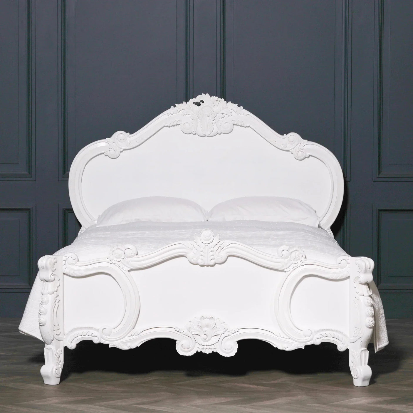 White carved wooden bed frame with ornate details against dark wall