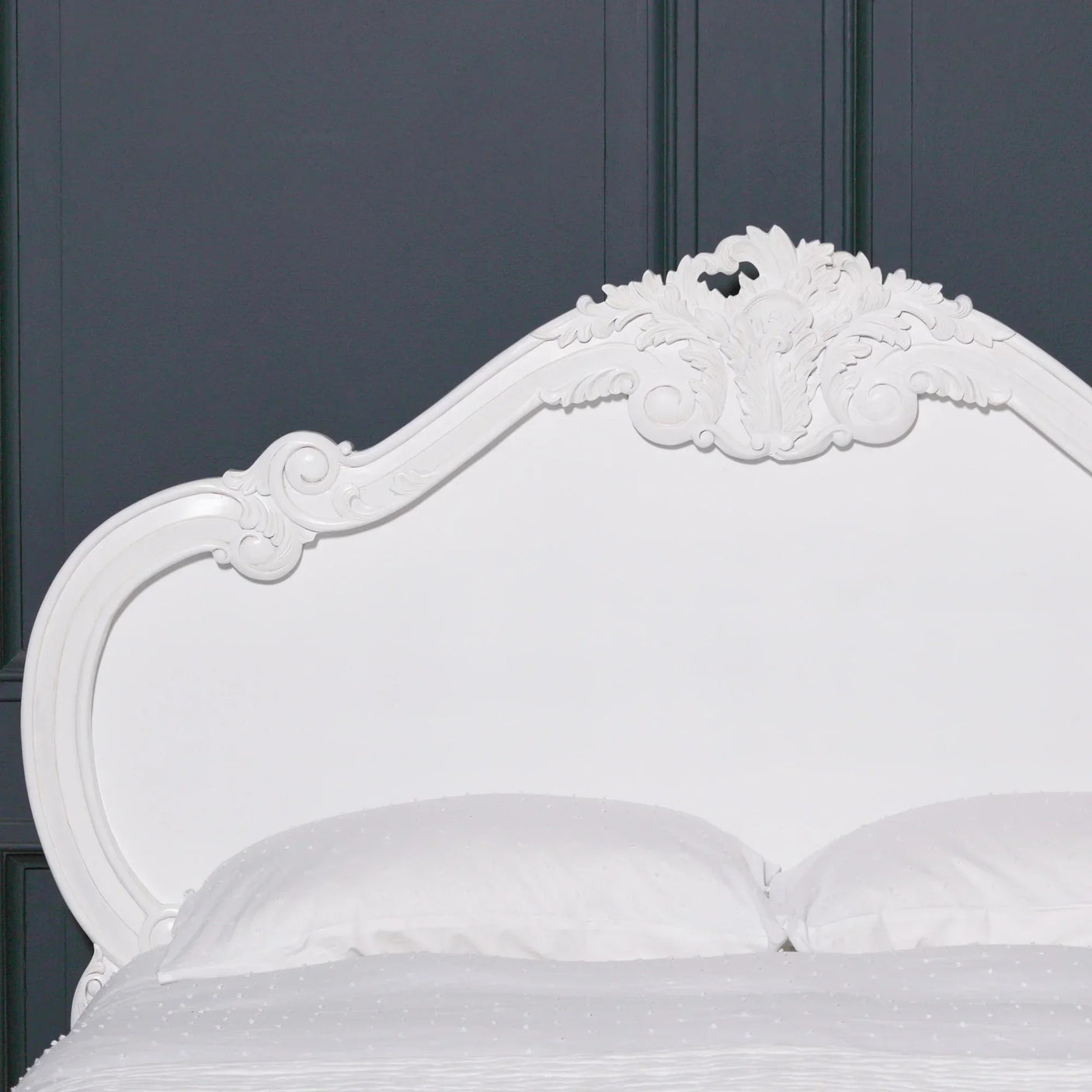White carved wood bed frame headboard with ornate detailing against dark panel wall