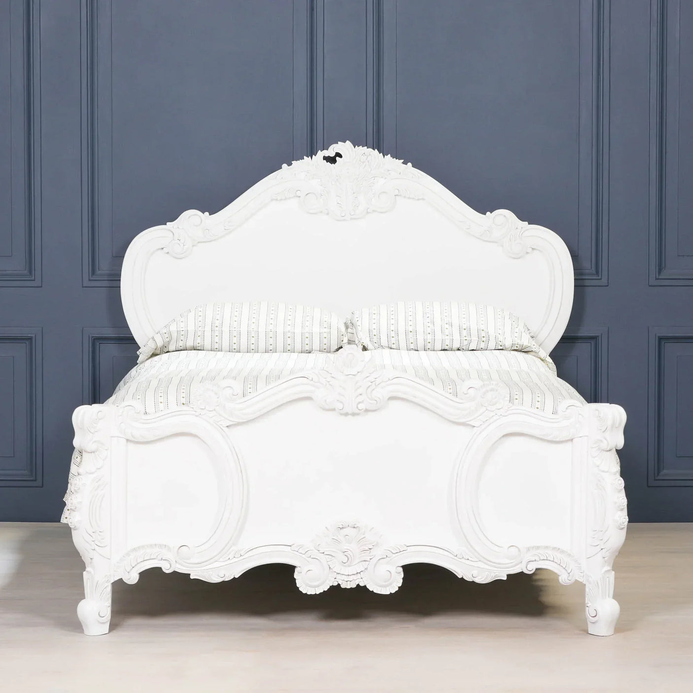 White carved wooden bed frame with ornate detailing against dark panelled wall