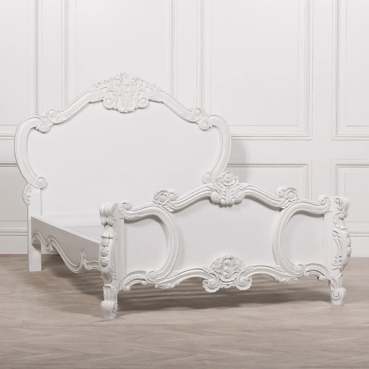 White carved wooden bed frame with ornate headboard and footboard on wood flooring