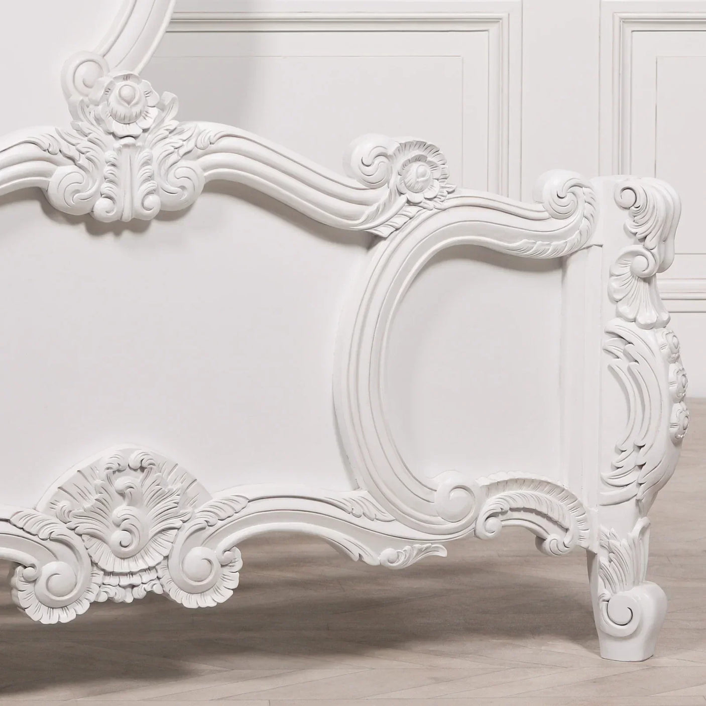 White carved wooden bed frame with ornate detailing and floral motifs on leg and panel