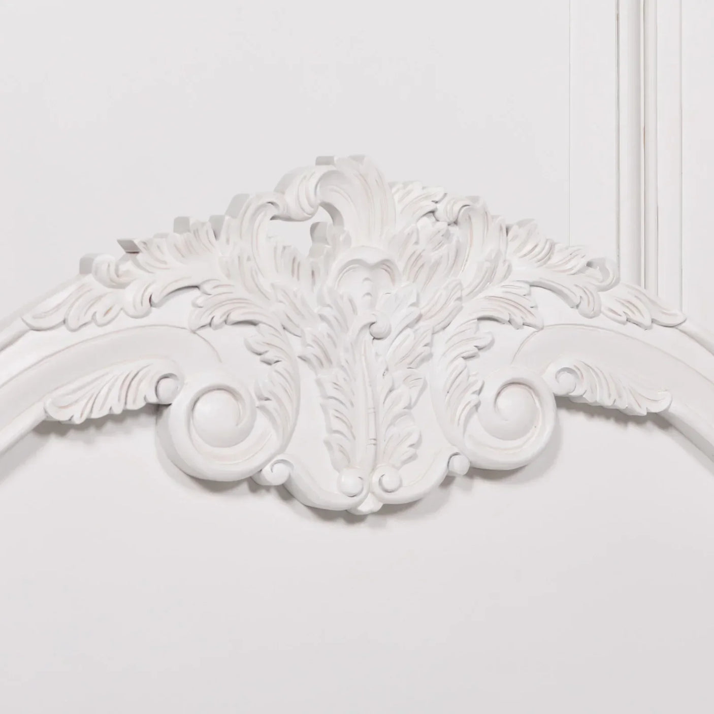 White ornate mirror frame with carved scroll and leaf details, close-up of top edge