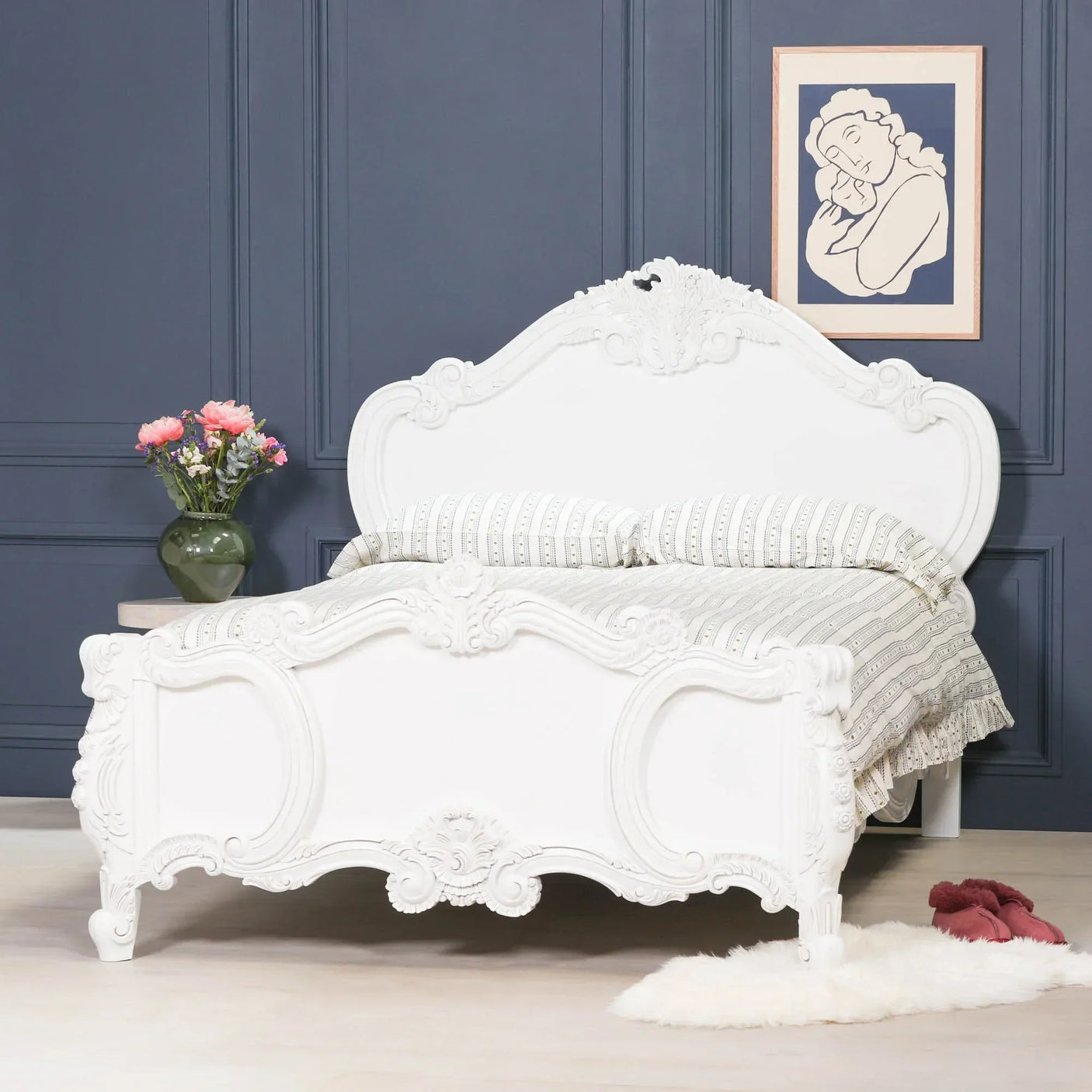 White carved wooden bed frame with ornate headboard against blue wall, striped bedding