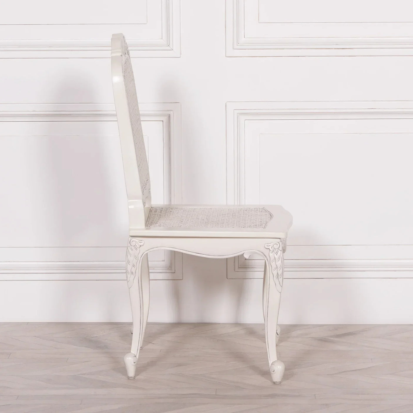 White dining chair with carved wooden legs and cane seat in side profile view