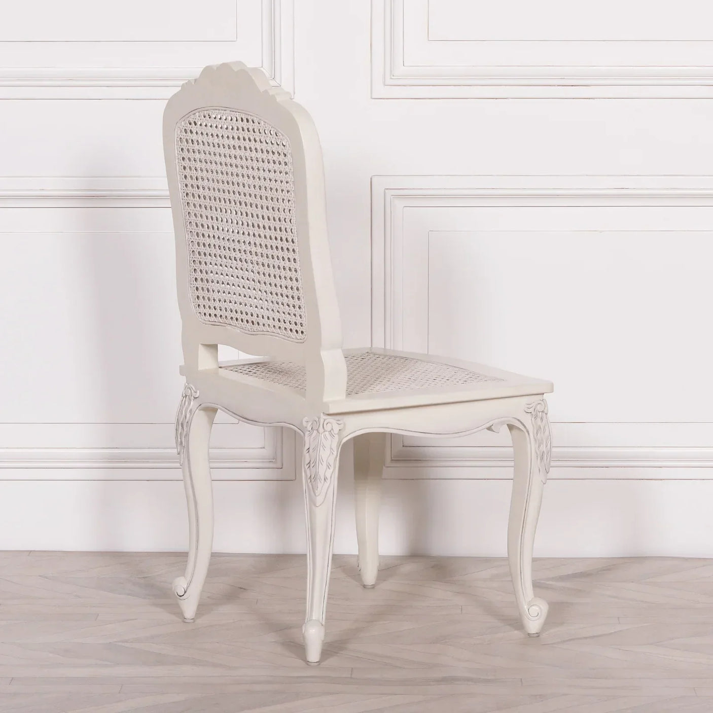 White rattan dining chair with curved legs and cane backrest against white paneled wall