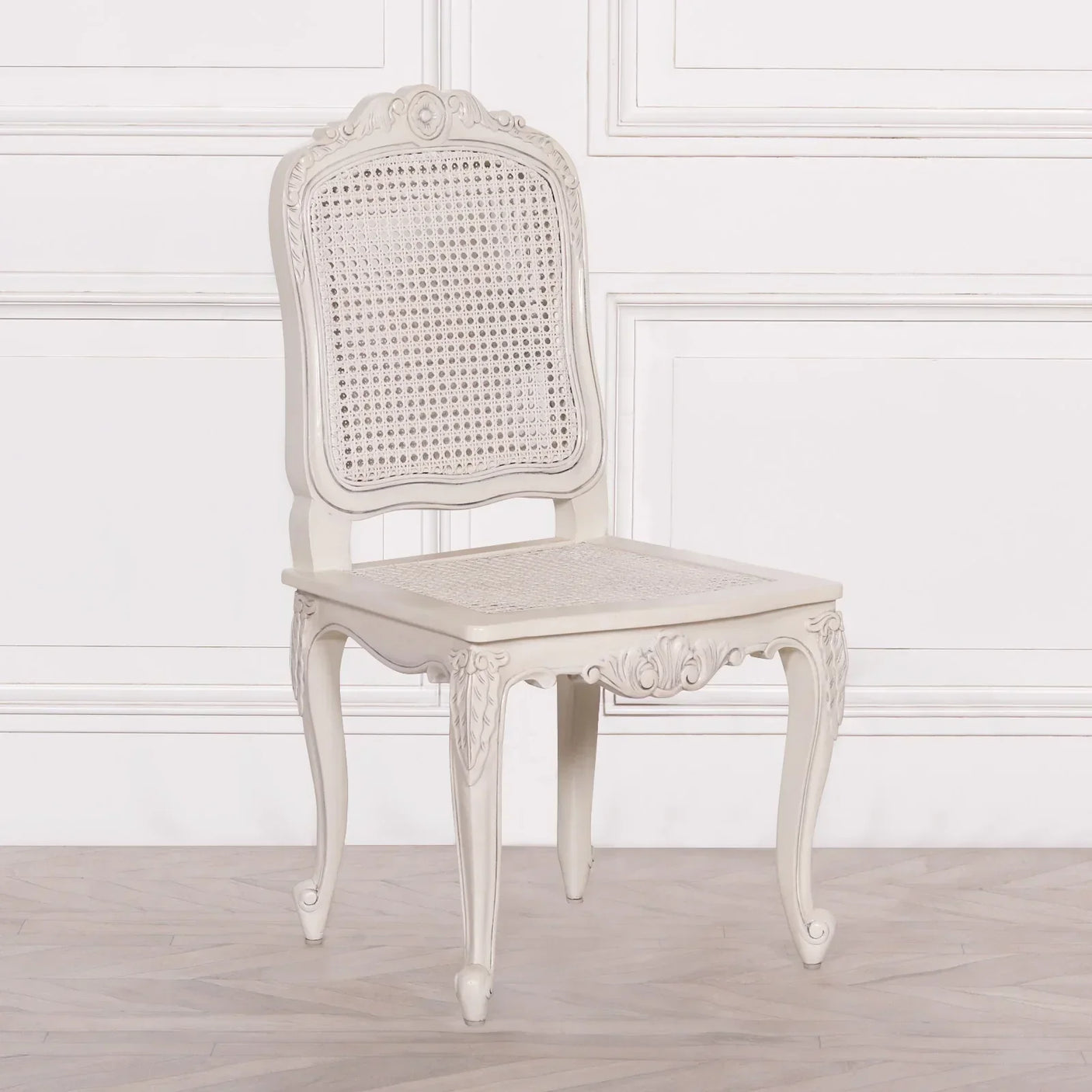 Cream carved wooden dining chair with cane seat and backrest on wooden floor