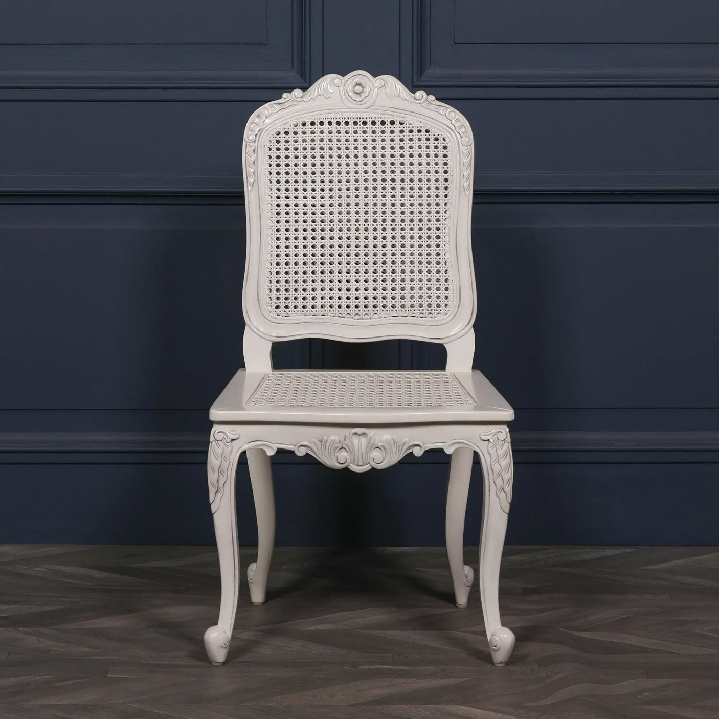 White cane dining chair with carved wooden frame against navy wall on parquet floor
