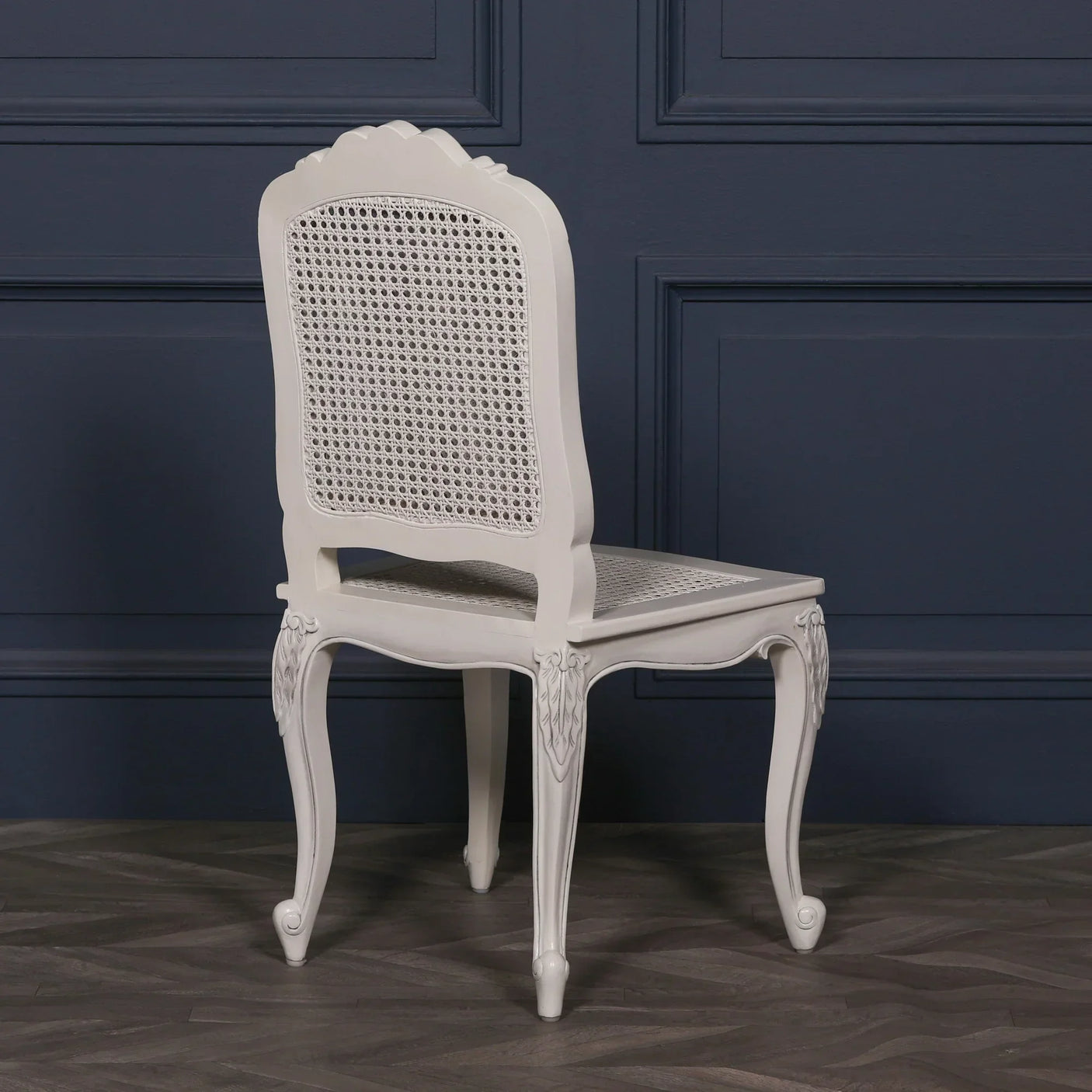 White rattan dining chair with carved legs and cane backrest, angled view
