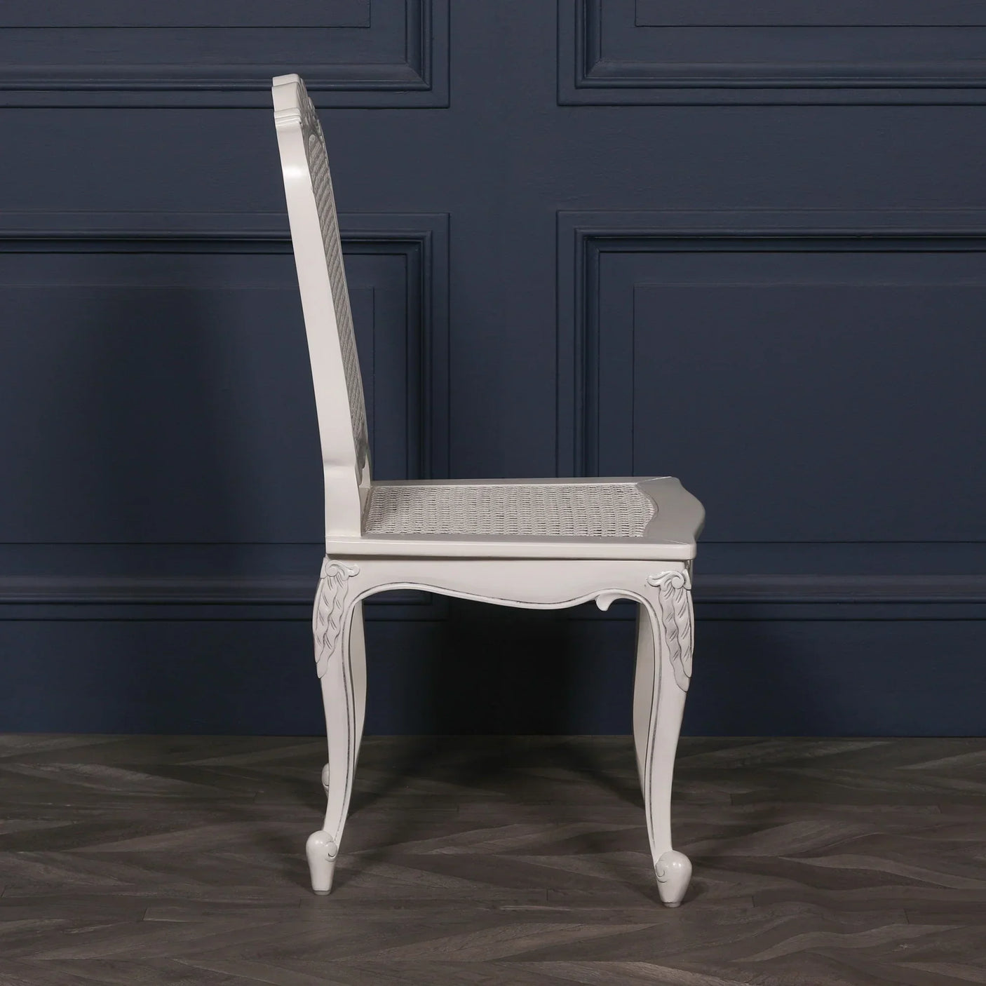 Side view of white dining chair with carved wooden legs and rattan seat on wood floor
